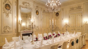 Un menjador formal amb una taula llarga preparada per a dinar, decoracions murals ornamentals i un penjador.