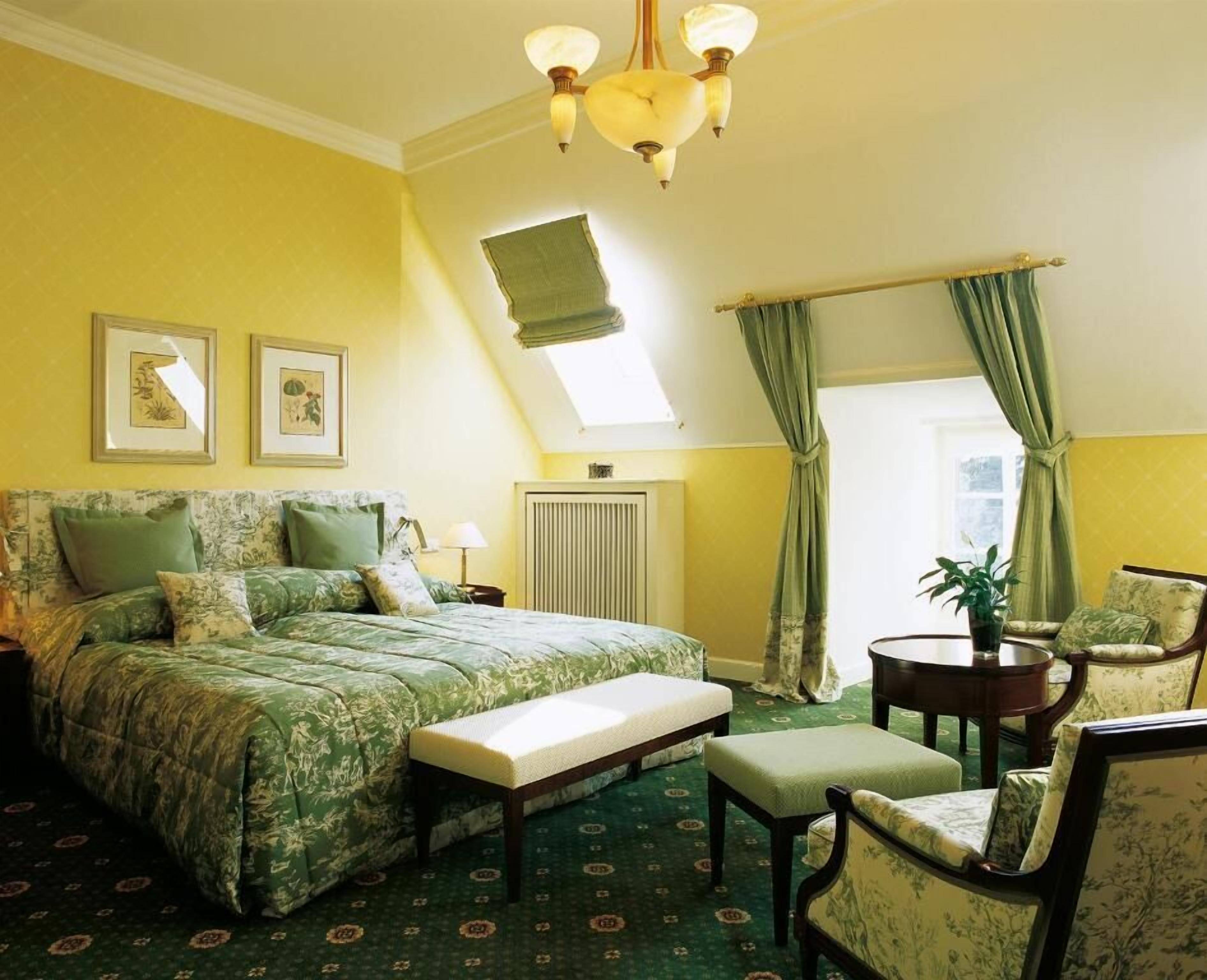 Een kamer met een bed, een bankje, een stoel, een tafel en een plafondventilator.