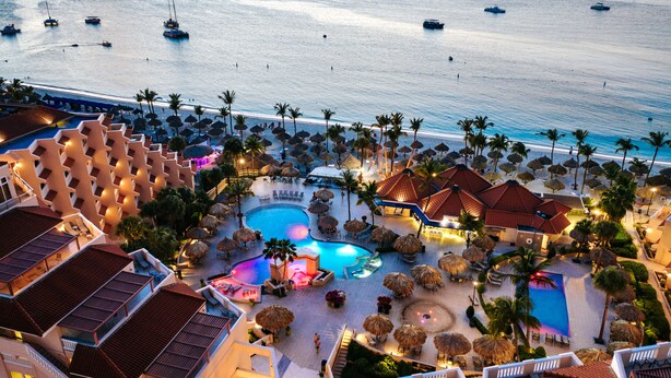 Un resort con varias piscinas, palmeras y vistas a la playa.