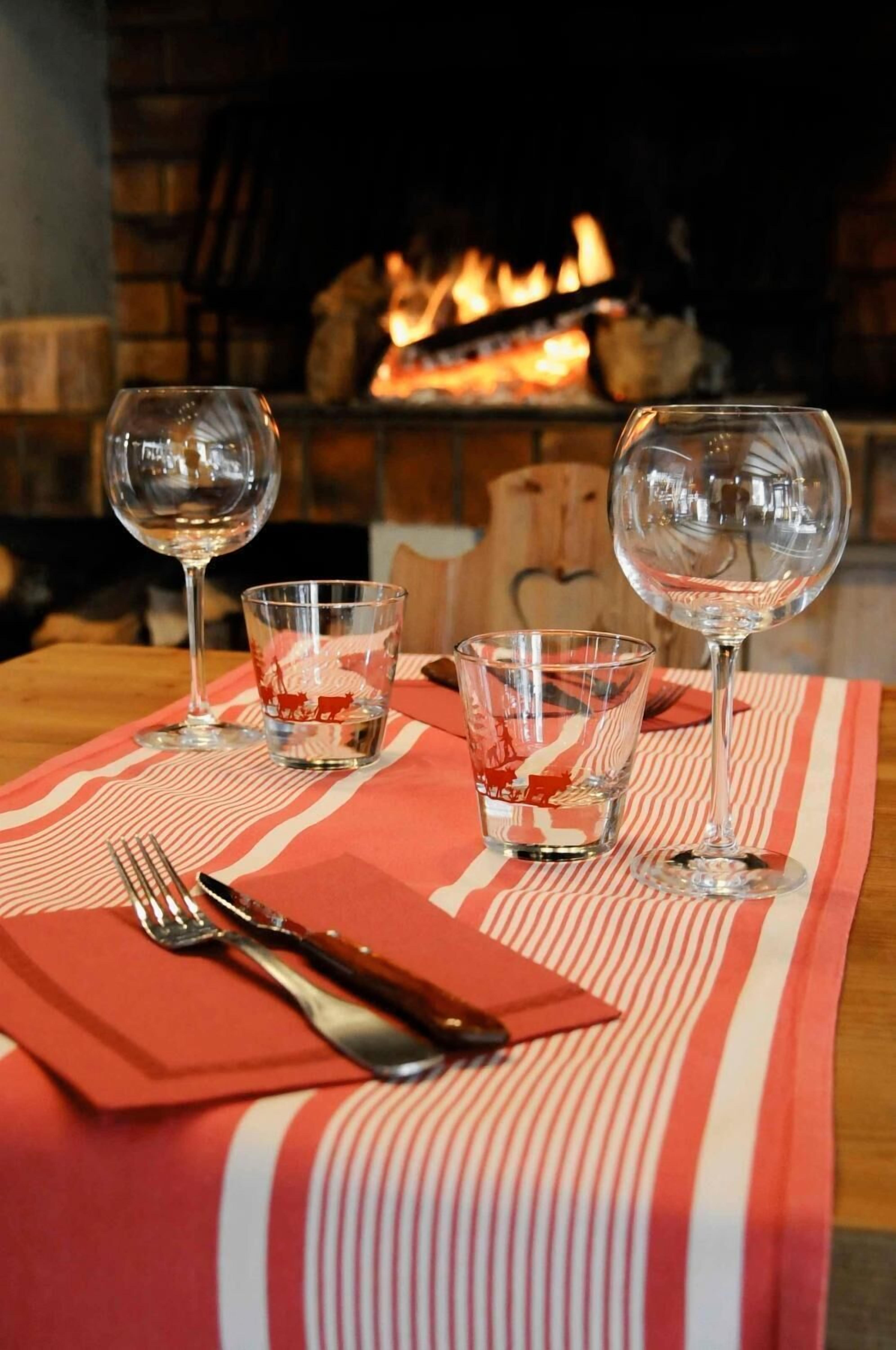 A table set with wine glasses and cutlery on a striped tablecloth, with a fireplace in the background.