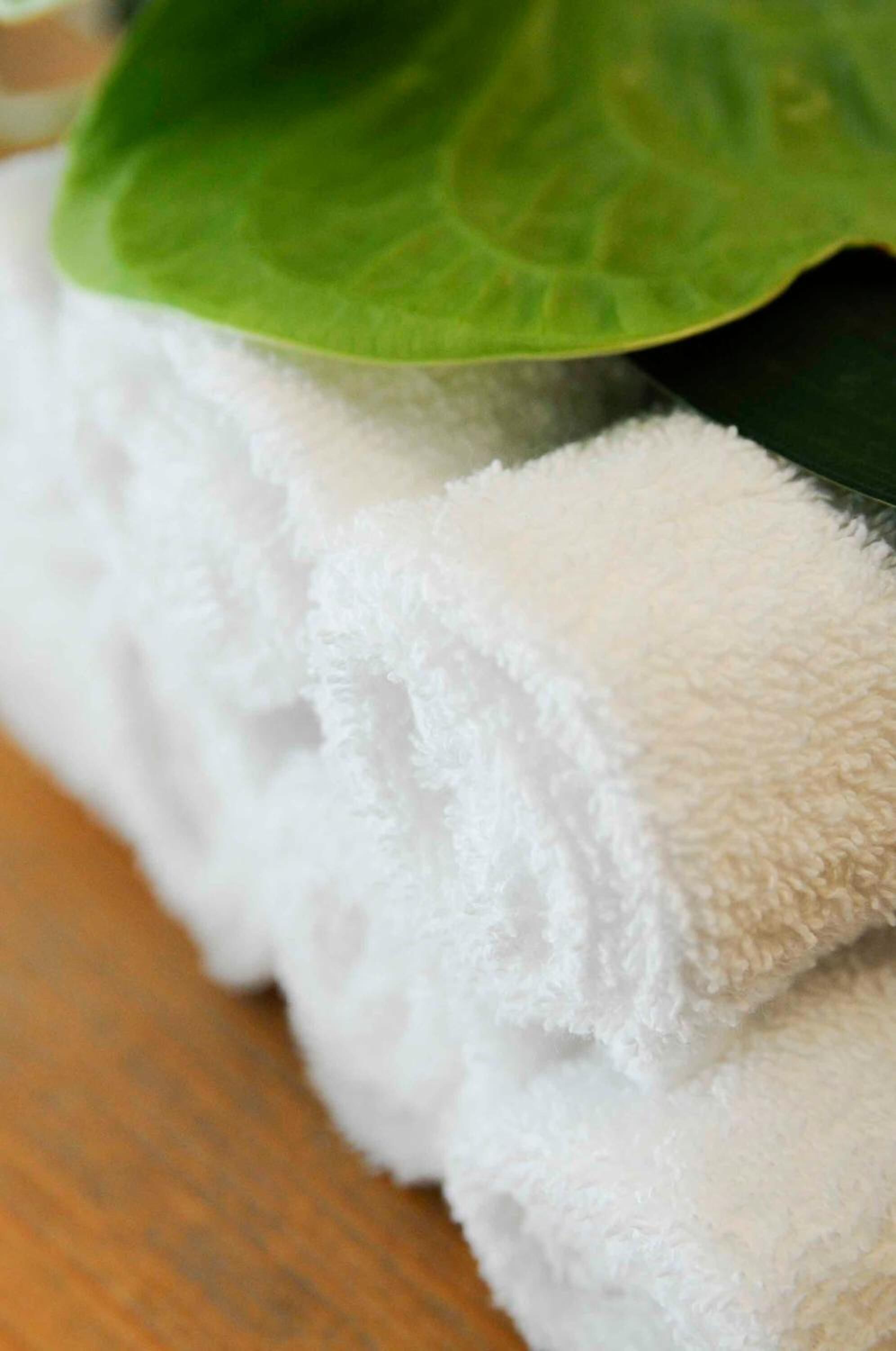 A white towel with a green leaf on top, placed on a wooden surface.