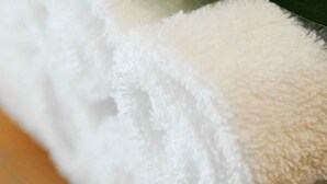 Una toalla blanca con una hoja verde encima, sobre una superficie de madera.