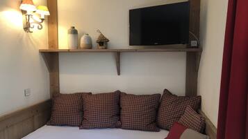 Un dormitorio con cama, almohadones estampados, televisor montado y lámparas de pared.