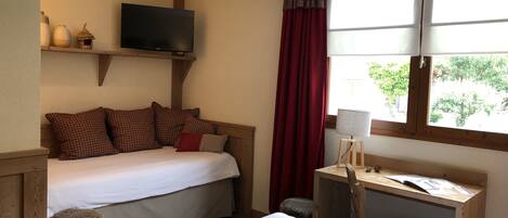A bedroom with a bed, a desk, a chair, a television, and a window with curtains.