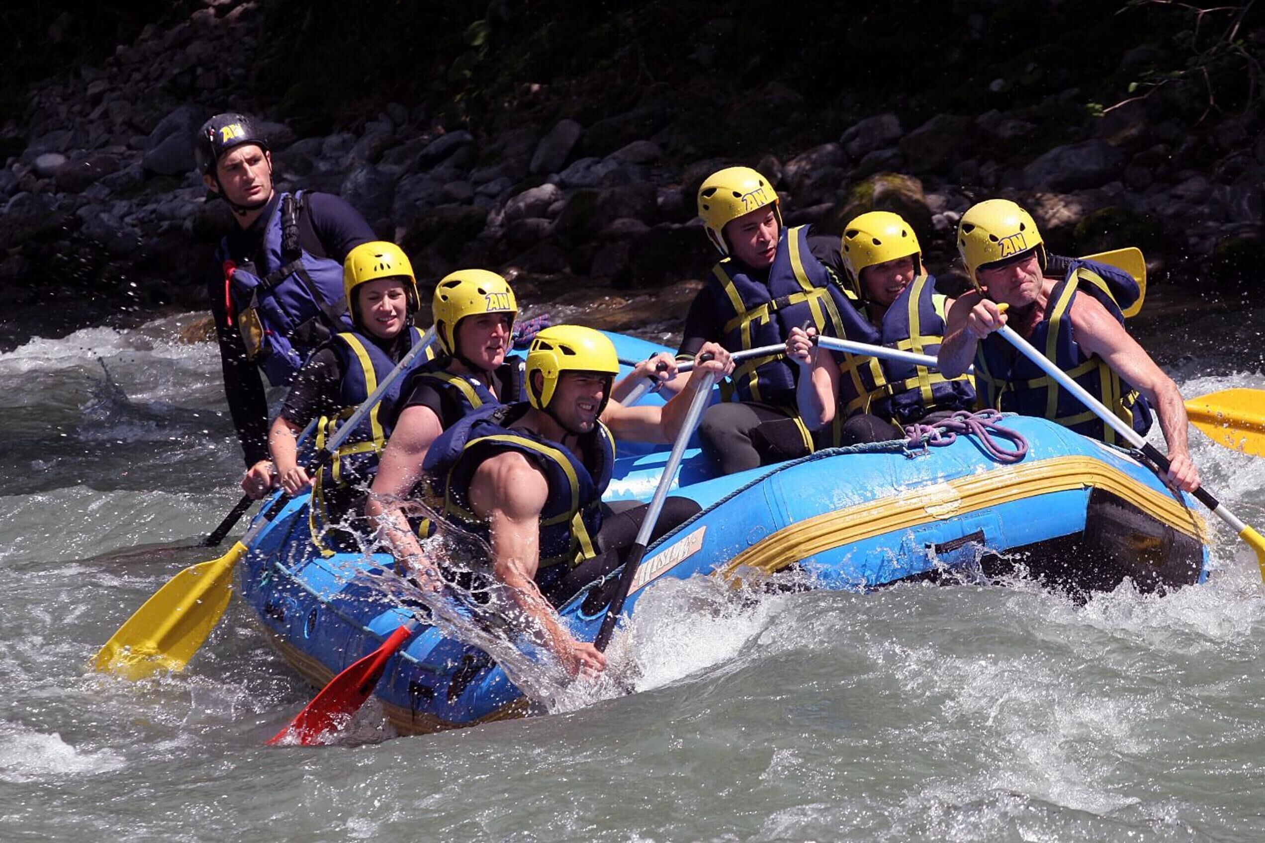 A group of people in a blue inflatable raft navigating through a river.