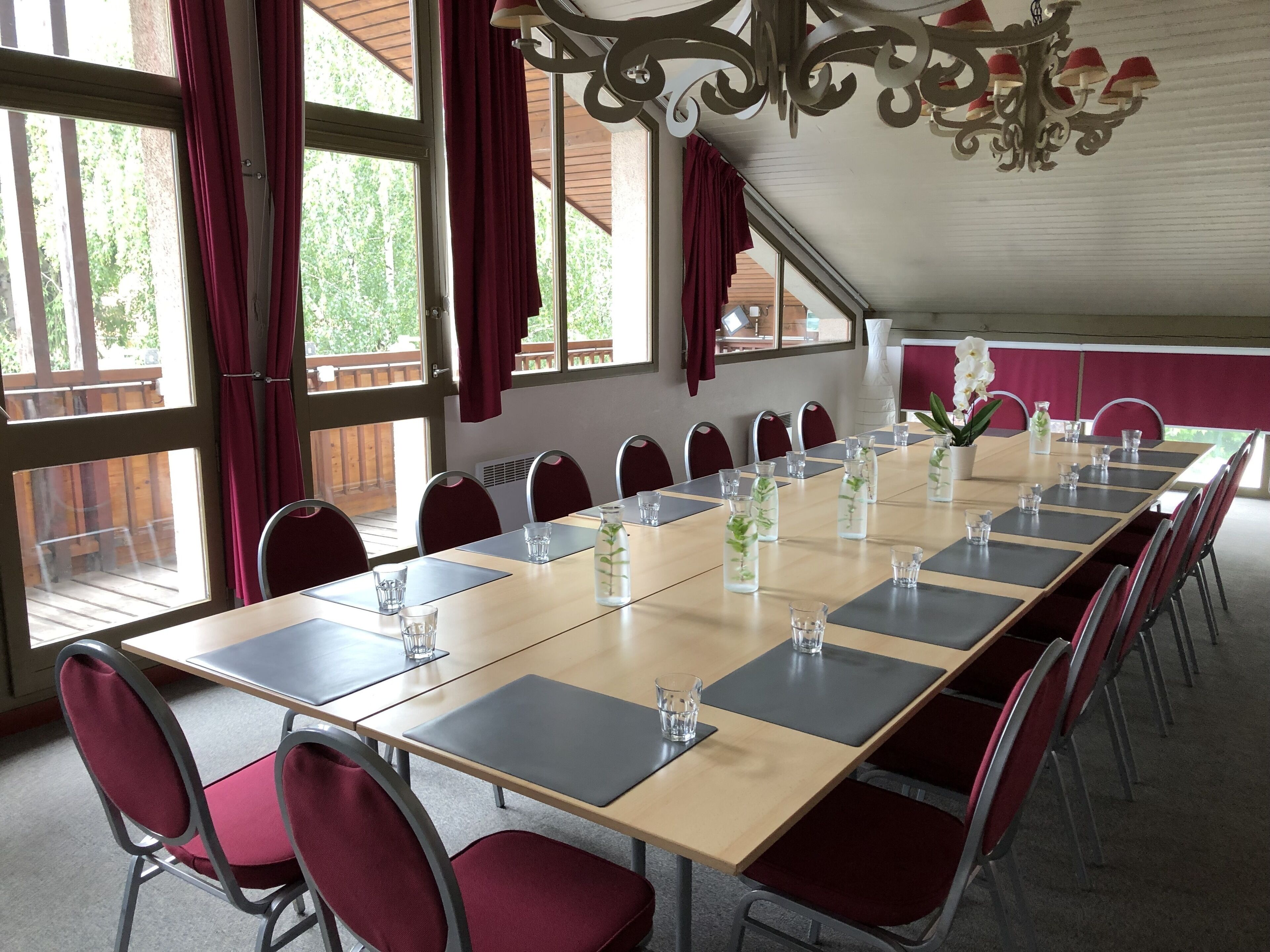 Een vergaderruimte met een lange tafel, rode stoelen en grote ramen voorzien van gordijnen.