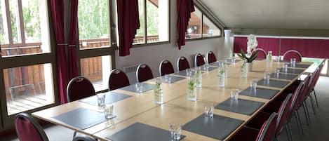 A conference room with a long table, red chairs, and large windows with curtains.