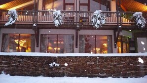 Un edificio imbiancato dalla neve, con un balcone decorato da palle di neve e rami, ampie finestre e un muro di pietra di fronte.