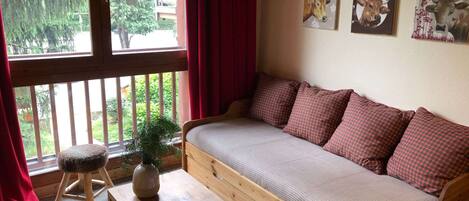 A cozy room with a wooden sofa, a small stool, and a book on a wooden table. There are three wall-mounted pictures of cows.