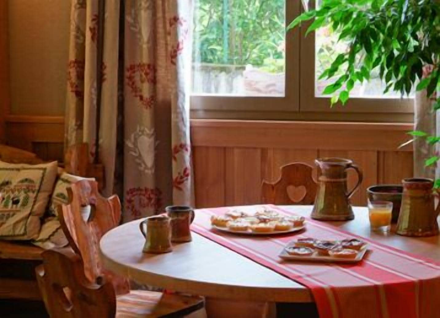 Una mesa de comedor con mantel rojo, dos jarras, un vaso de jugo de naranja y un plato de pasteles.