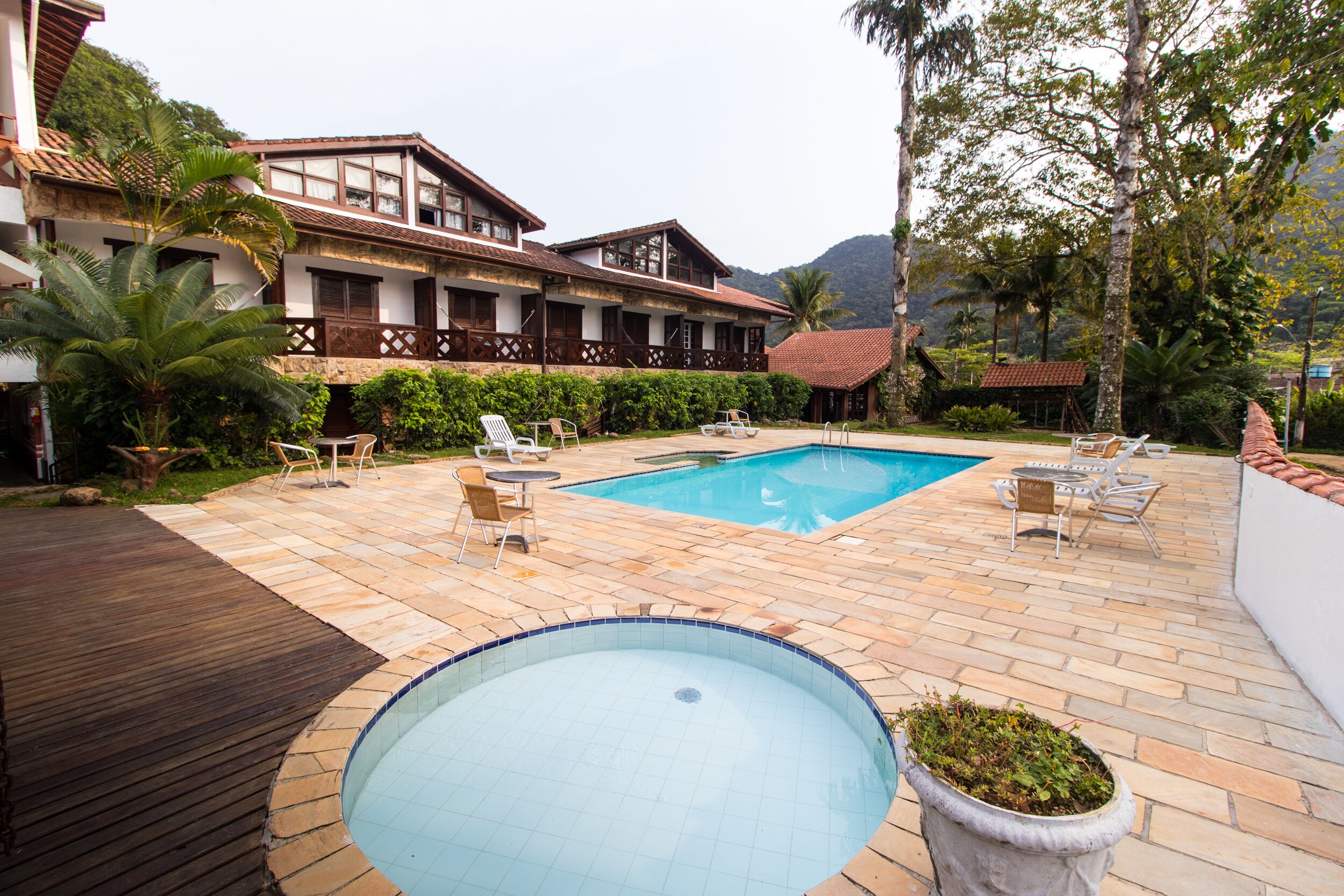 A pool area with lounge chairs and a small pool, surrounded by a wooden deck and a building with a tiled roof.