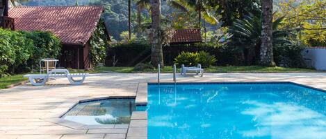 A swimming pool with a tiled deck, surrounded by lush greenery and palm trees.
