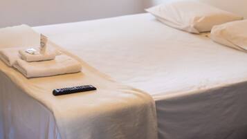 Habitación de hotel con una cama bien hecha, un control remoto y una toalla sobre la cama.