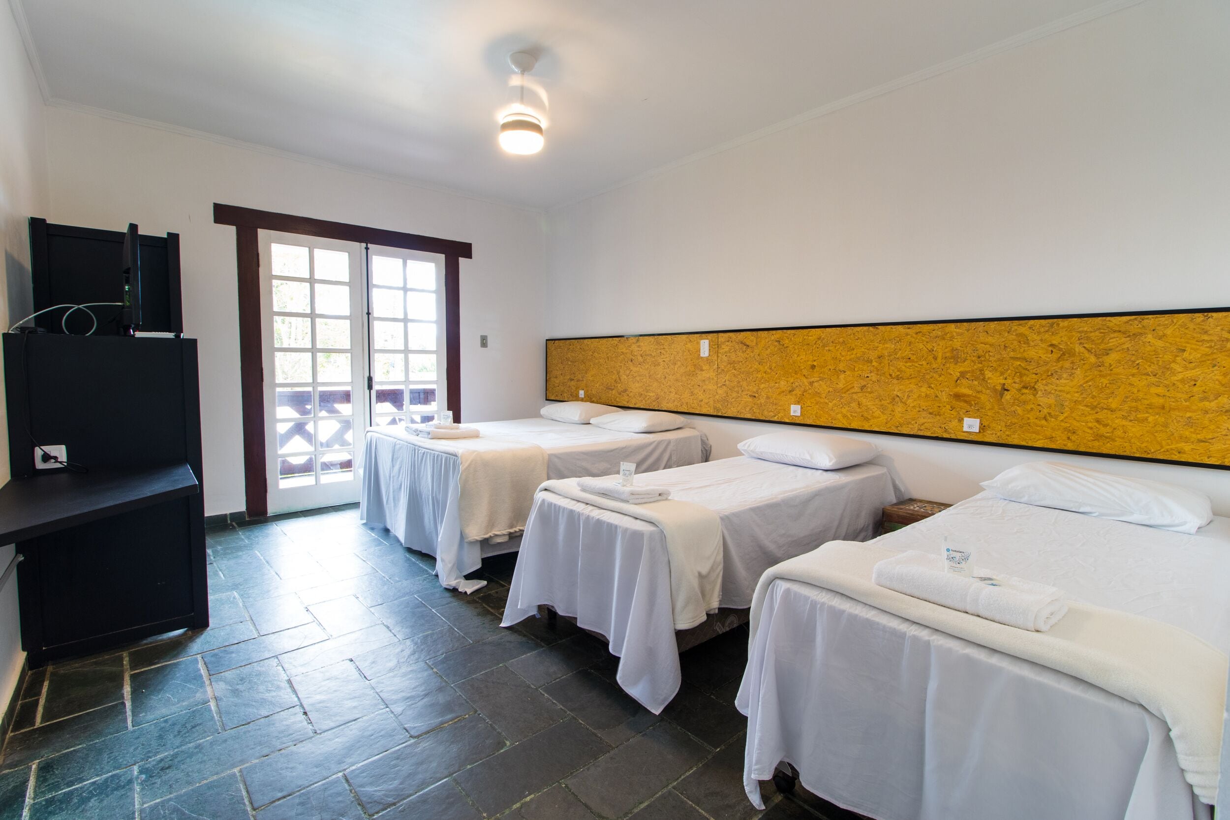 A hotel room with two single beds, a TV, and a sliding door to the outside.