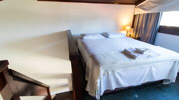 A neatly made bed with white linens and towels, a wooden chair, and a nightstand with a lamp.