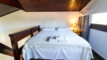 Una cama bien hecha con ropa de cama y toallas blancas, cabecera de madera y una mesita de noche con lámpara.