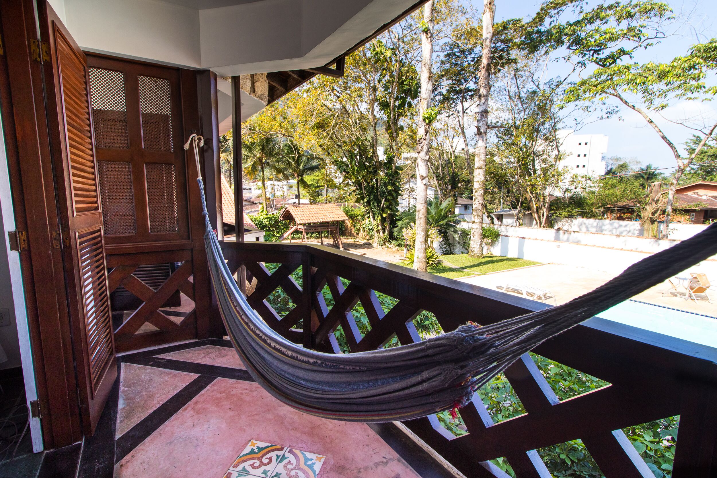 Una hamaca en un balcón con vistas a una piscina y follaje circundante.