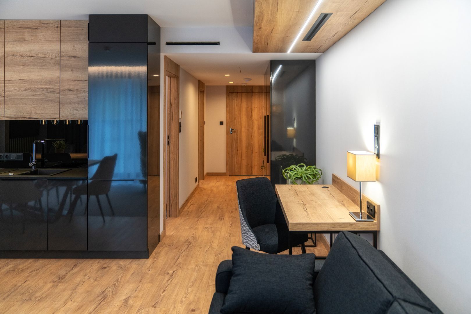 Een moderne keuken met donkere kastjes, een houten eettafel met stoelen en een zithoek met een bank.