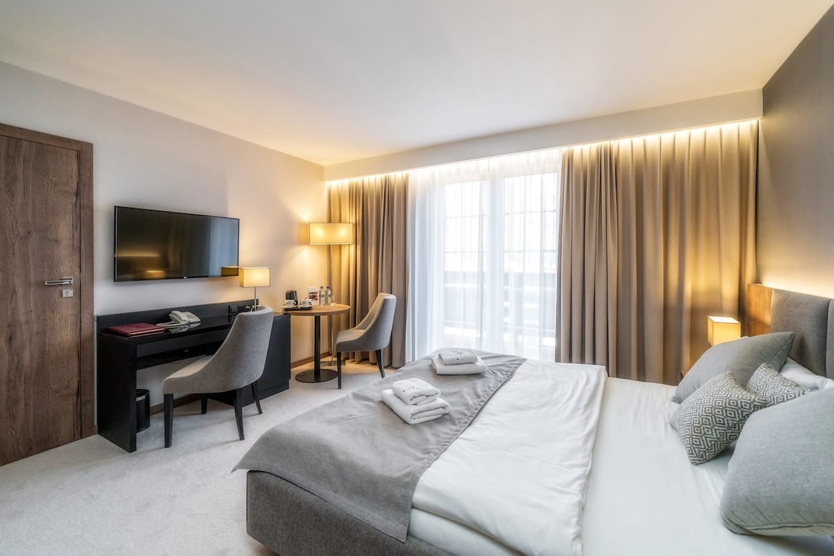 Habitación de hotel con cama, escritorio, silla, televisor y cortinas.
