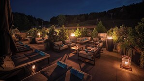 An outdoor seating area with lounge chairs and tables, surrounded by greenery and illuminated by ambient lighting. - Hotel Meta Resort & Vine SPA (Szczyrk)