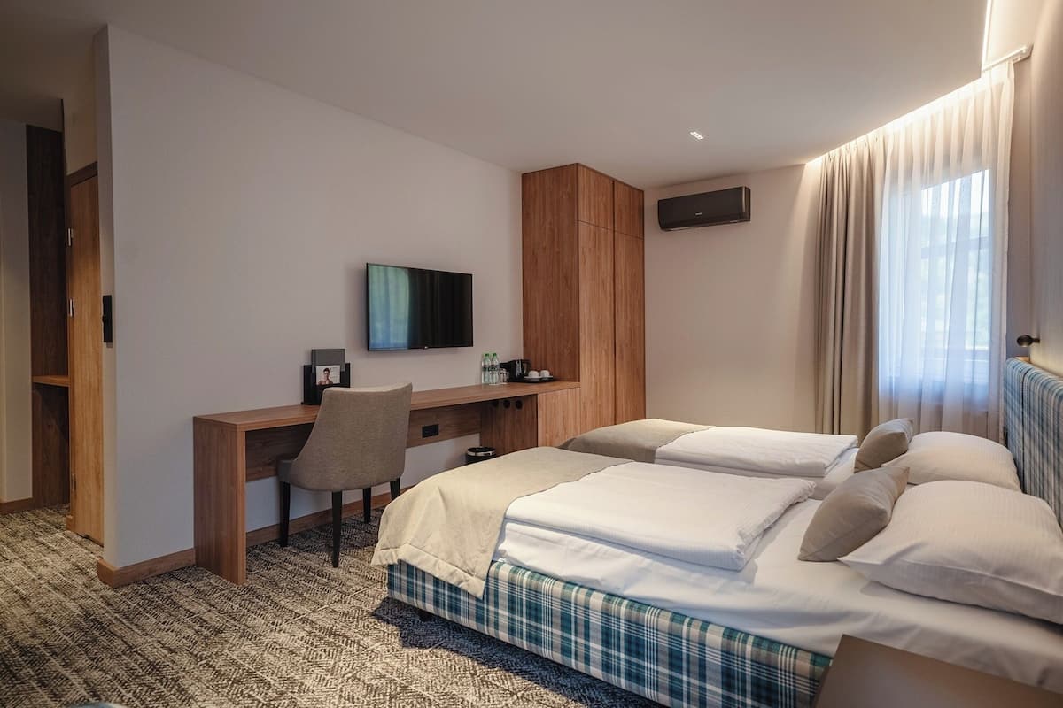 Habitación de hotel con dos camas, un escritorio, una silla, un televisor y una ventana con cortinas.