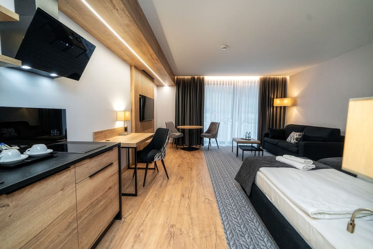 Una habitación de hotel moderna con un escritorio de madera, un sofá, una cama y un televisor montado en la pared.