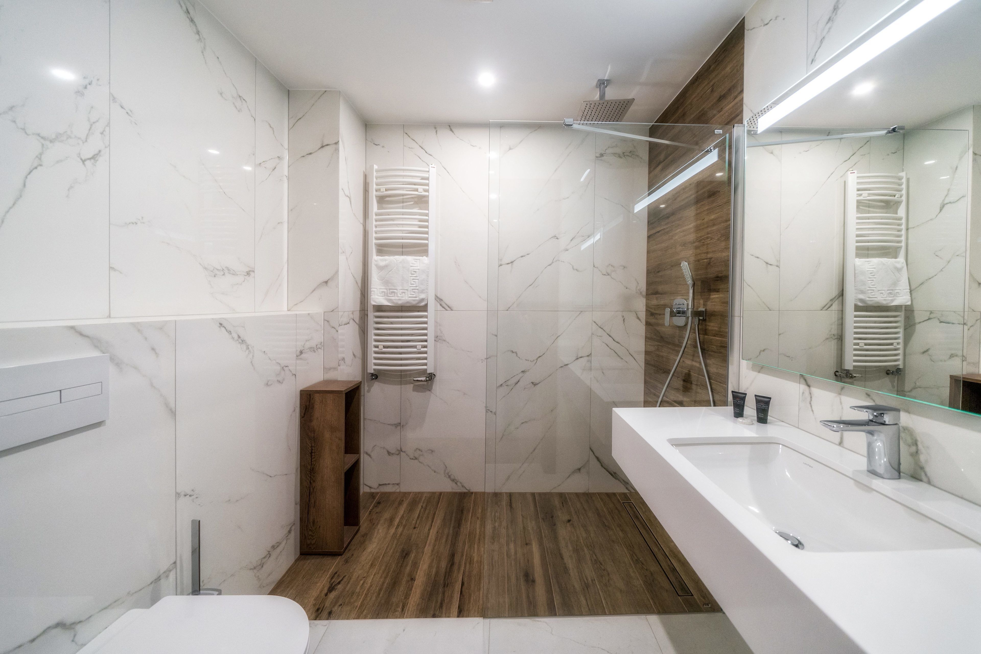 Une salle de bain moderne avec un grand miroir, des murs en marbre blanc, un plancher en bois et un espace douche.