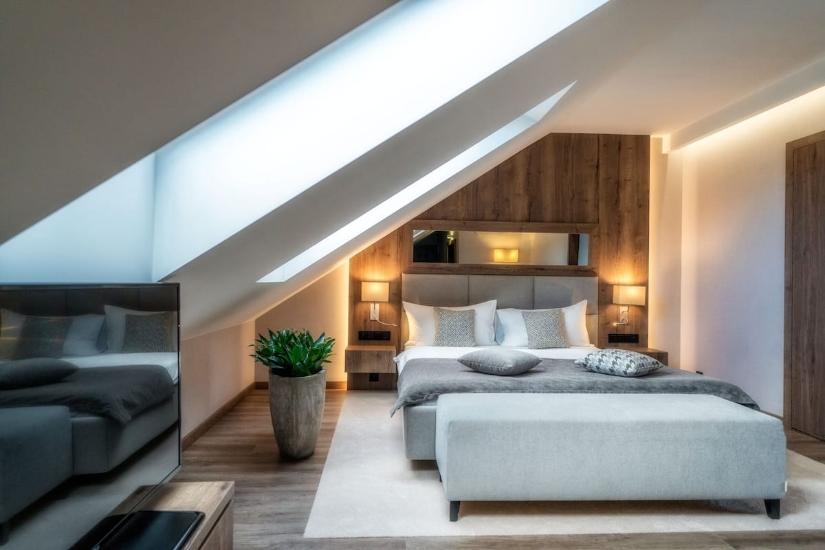 Un dormitorio moderno con techo inclinado, una cama grande, mesitas de noche y una planta en maceta.