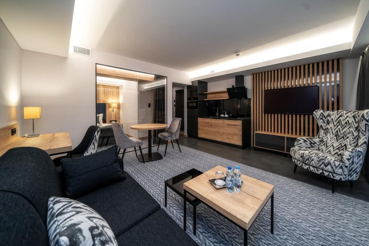 Una habitación de hotel moderna con sofá, una mesa de comedor, zona de cocina y alfombra estampada.