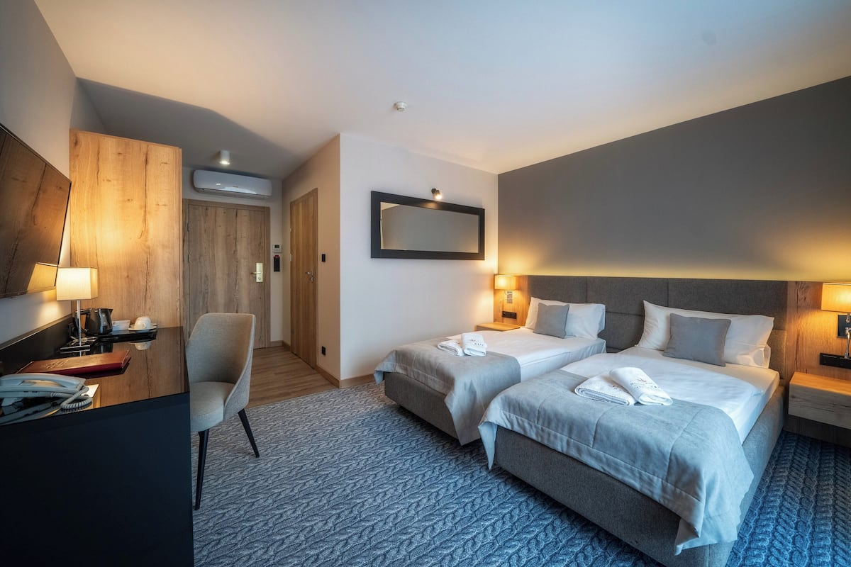 Habitación de hotel con dos camas, un escritorio, una silla, un espejo y aire acondicionado instalado en la pared.