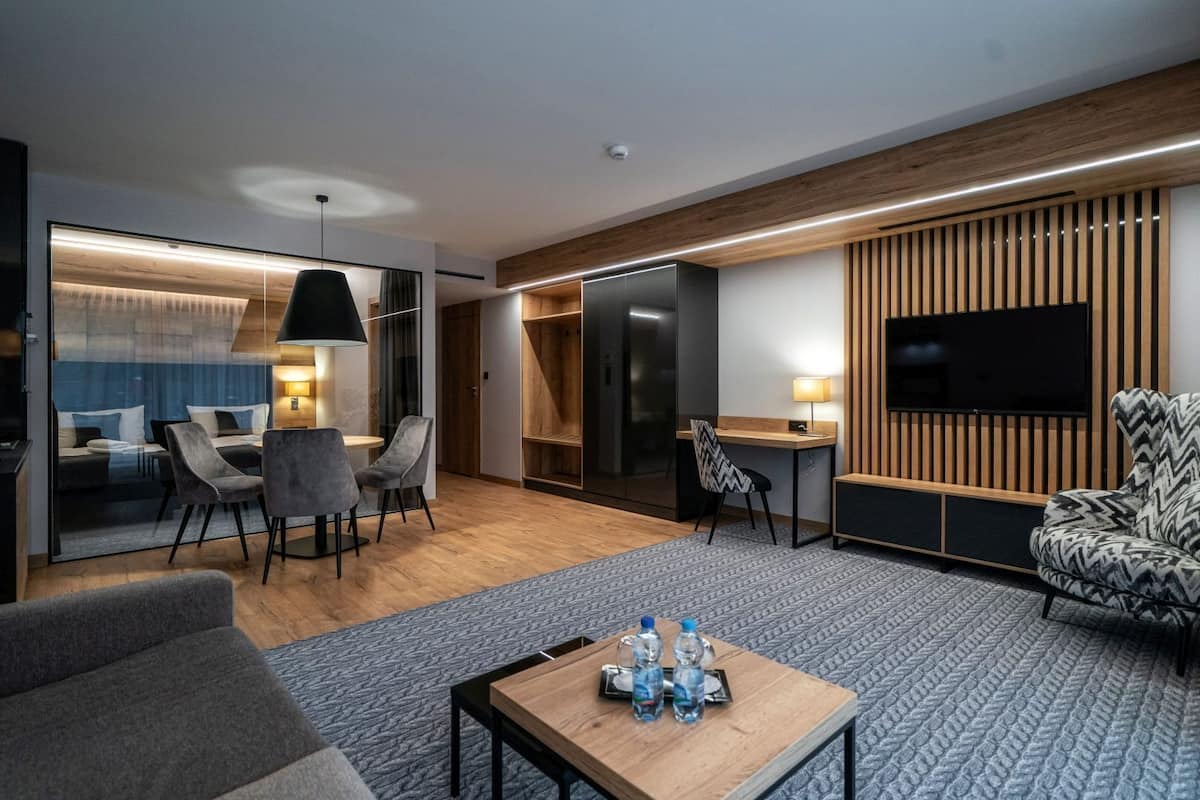 Una habitación de hotel moderna con sala de estar, comedor y televisor en la pared.