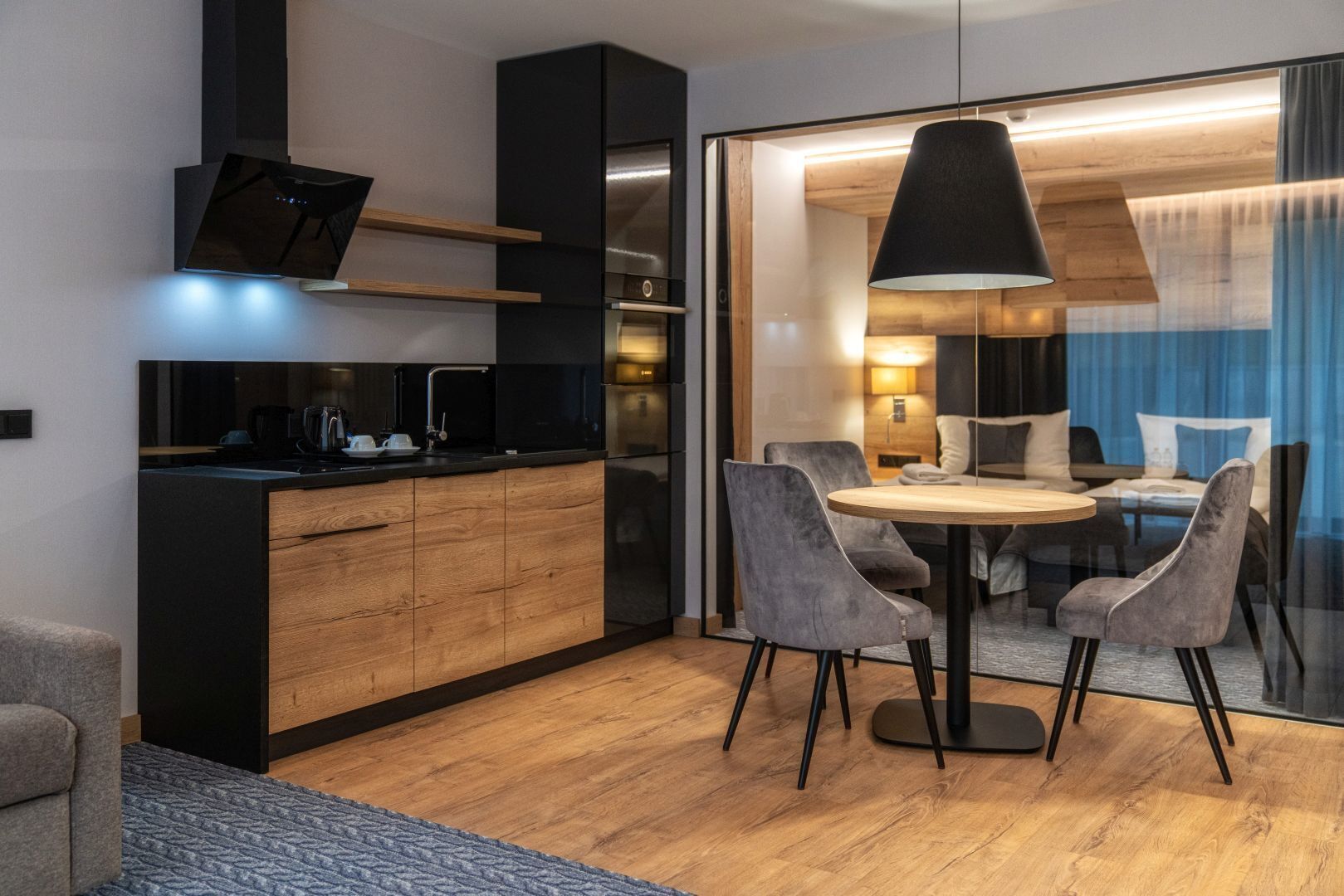 Una cocina moderna con estufa integrada, un comedor con mesa redonda y cuatro sillas, y un amplio ventanal con vista a la ciudad.