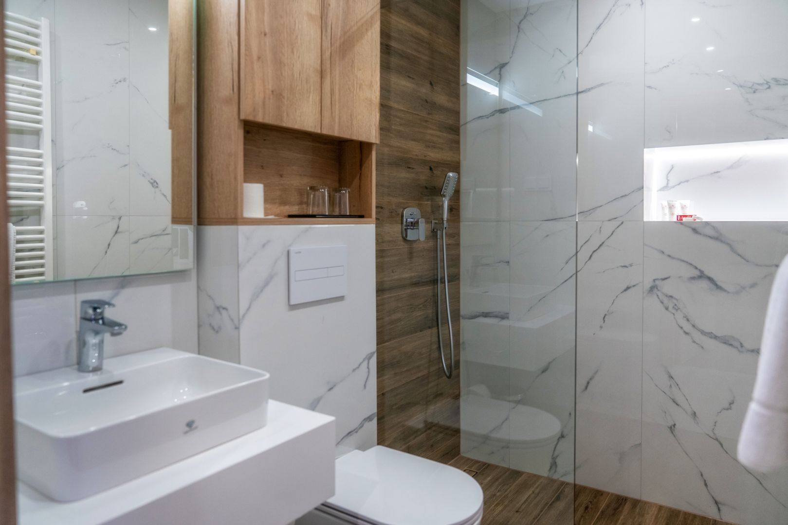 Un baño moderno con lavamanos de mármol, armario de madera y cabina de ducha con mampara de vidrio.