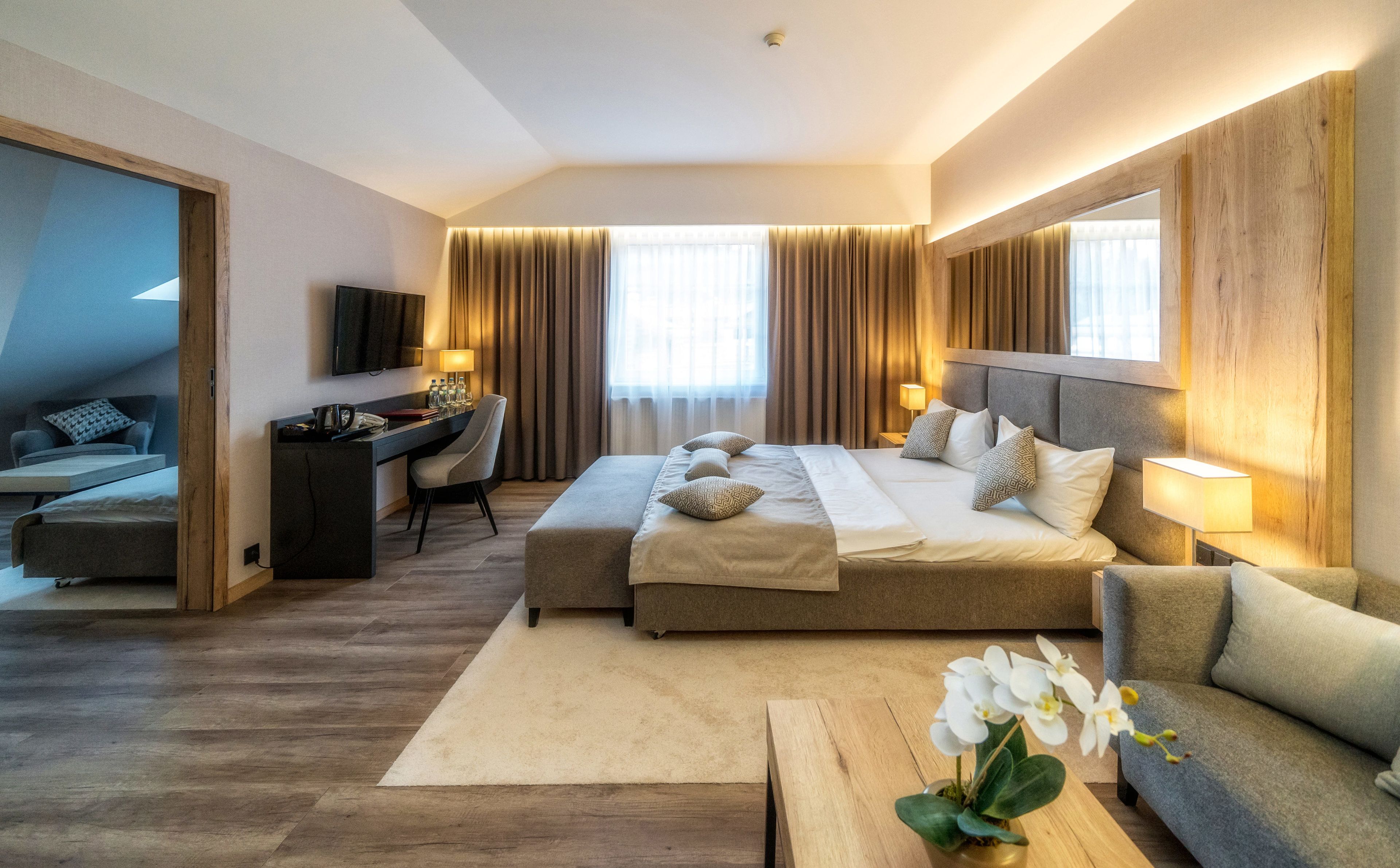 A hotel room with a large bed, a desk, a chair, a TV, and a sofa.