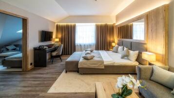 A hotel room with a large bed, a desk, a chair, a TV, and a sofa.