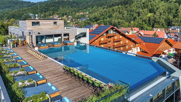 A modern hotel with a rooftop infinity pool, wooden deck seating, and a view of the surrounding forested hills. - Hotel Meta Resort & Vine SPA (Szczyrk)