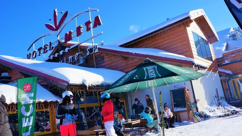 Un hôtel avec un panneau indiquant la présence d’une piste de ski, des places assises en plein air et du matériel de ski.
