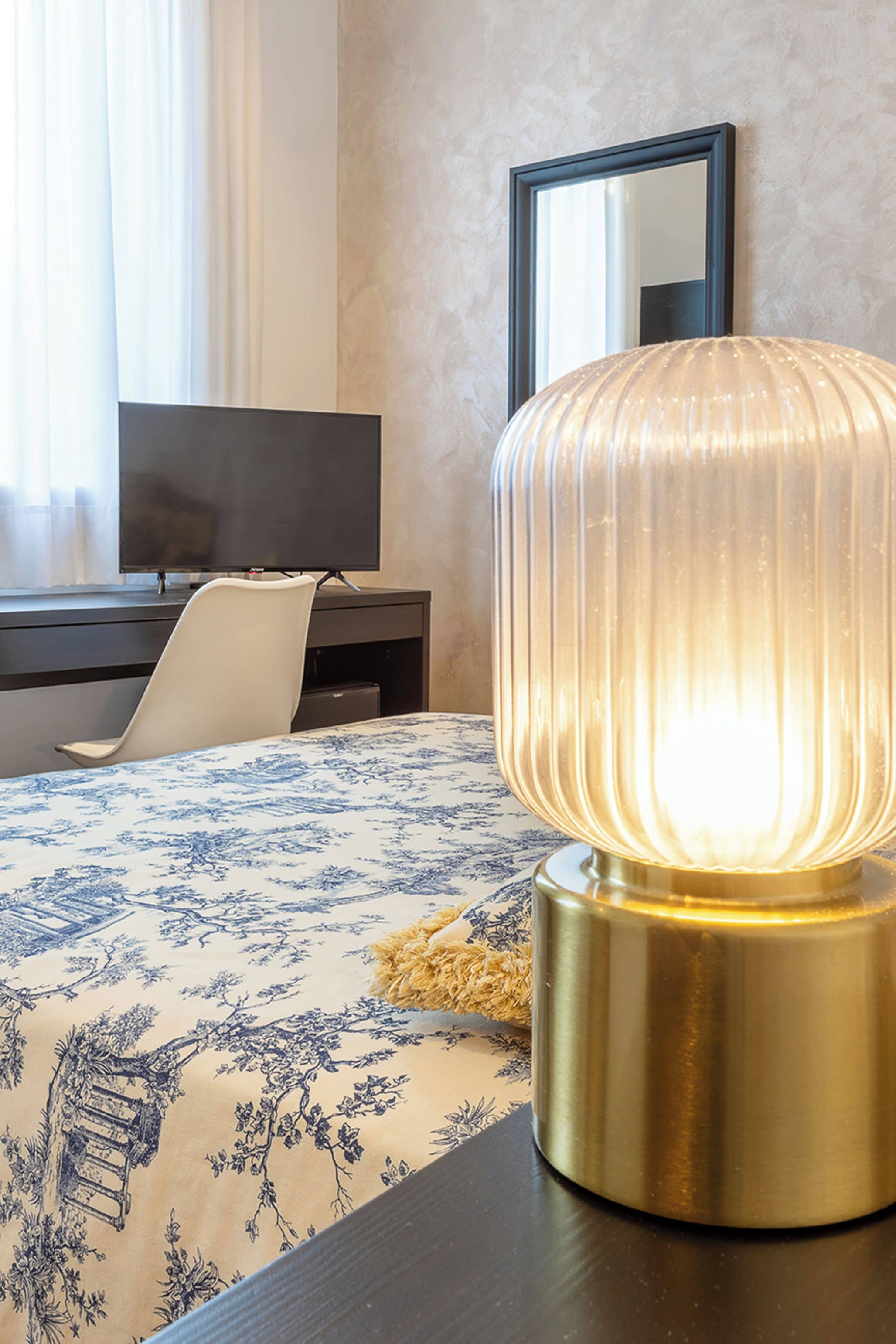 A hotel room with a bed, a desk, a chair, a television, and a wall-mounted mirror.