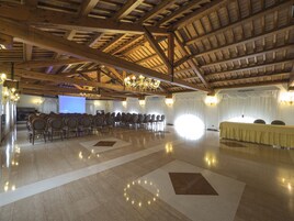 Un salón amplio con techo de madera alto y candelabros, asientos dispuestos y una pantalla de proyección.