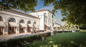 A building with arched windows and outdoor seating, surrounded by a well-maintained garden. - Villa Braida (Mogliano Veneto)