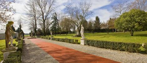 A pathway lined with statues and a red carpet, leading through a park with trees and a clear sky.