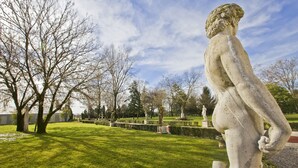 Une statue dans un parc aux pelouses et aux arbres soigneusement entretenus.