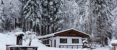 A wooden cabin with a sloped roof, surrounded by snow-covered trees.