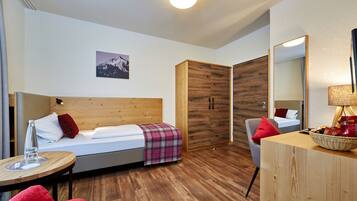 Ein modernes Hotelzimmer mit einem hölzernen Bett, einem kleinen Tisch mit einem Glas, einem Sessel, einem Kleiderschrank und einem Spiegel.