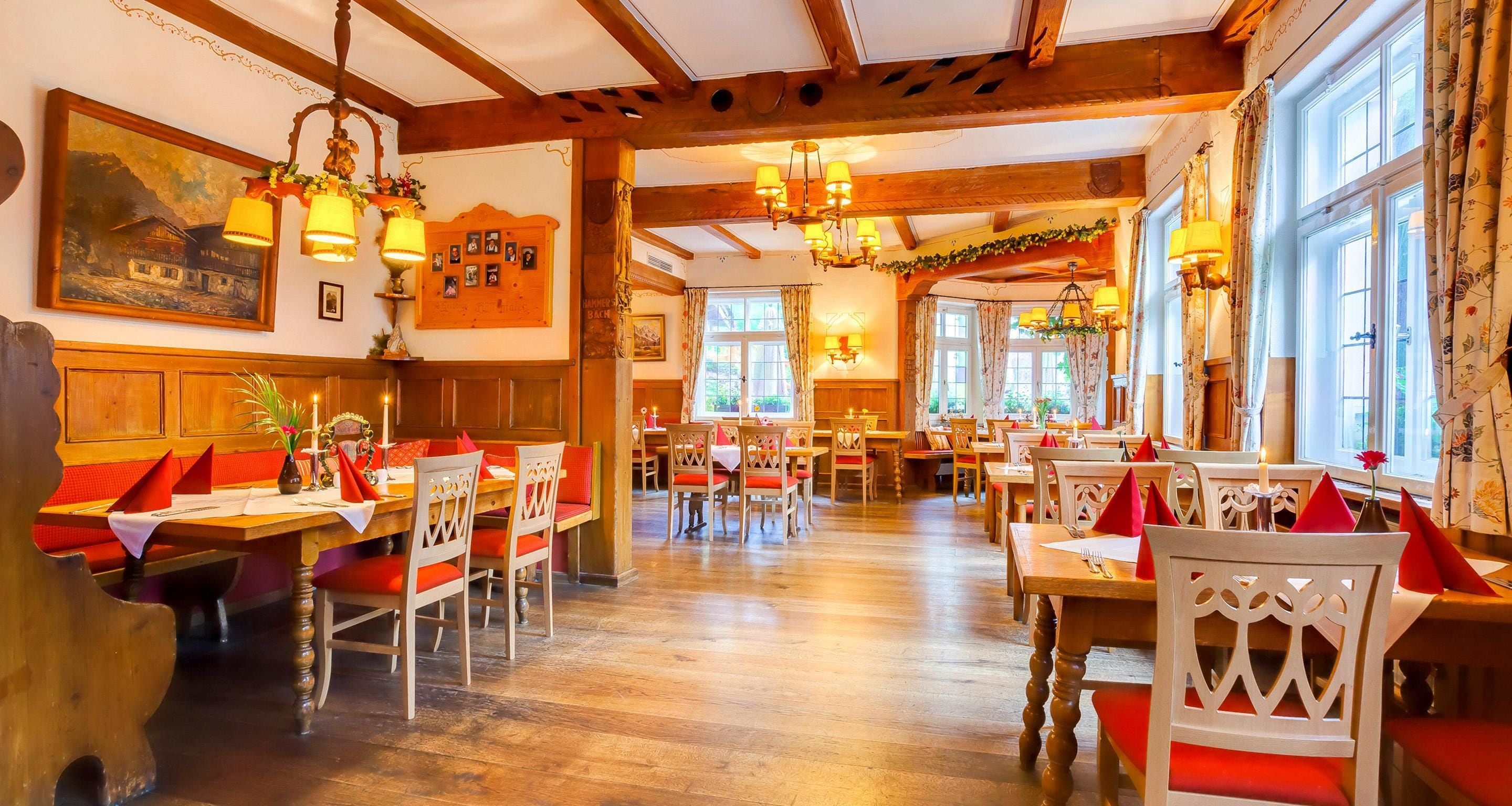Un restaurant avec des poutres en bois, de nombreuses tables et chaises, et des lampes suspendues.