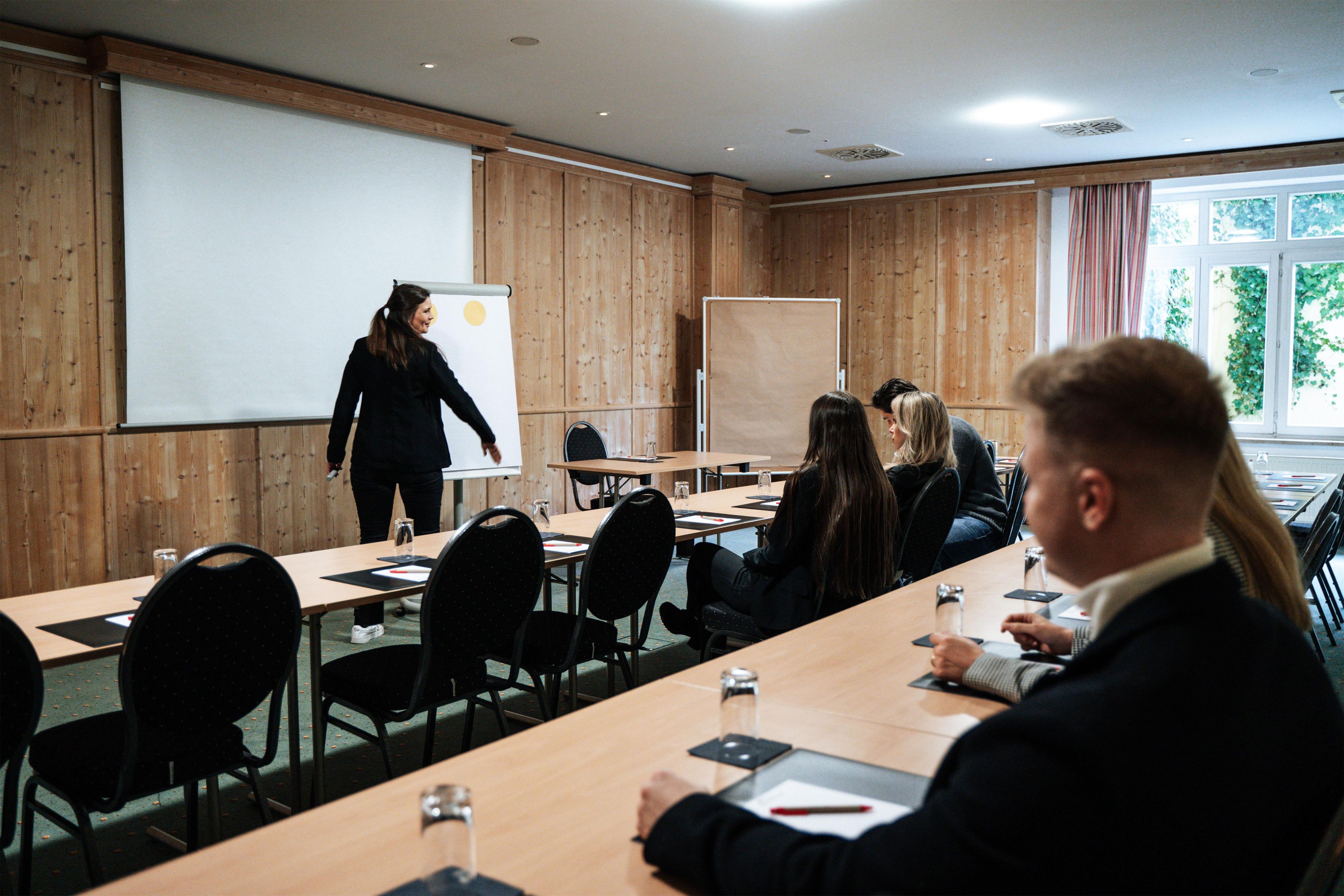 A conference room with a presentation screen, wooden panel walls, and a large window with curtains.
