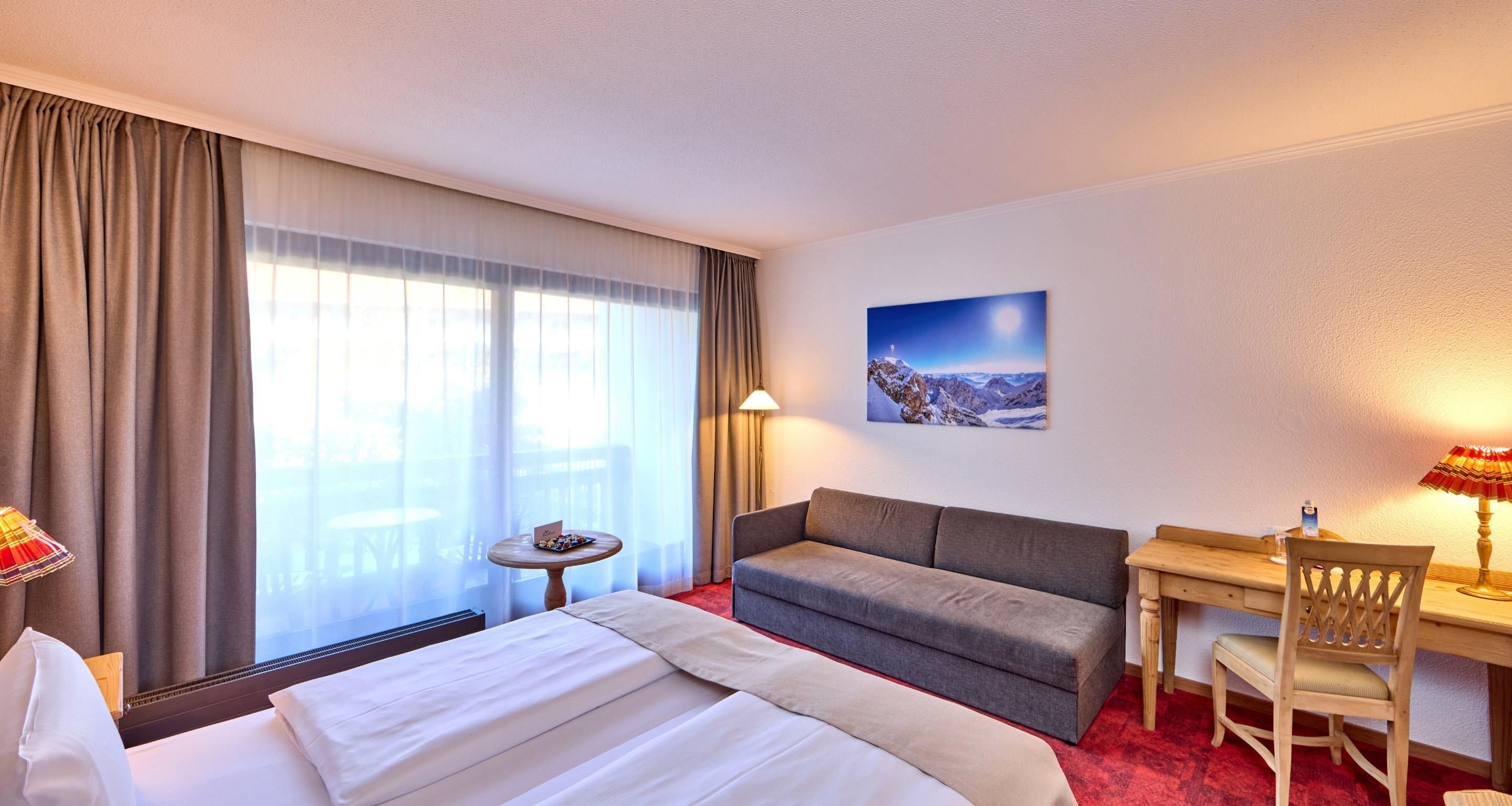 Ein Hotelzimmer mit Bett, Sofa, Schreibtisch, Stuhl, kleinem Tisch und einem Gemälde an der Wand.