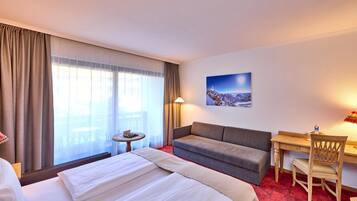 Ein Hotelzimmer mit Bett, Sofa, Schreibtisch, Stuhl, kleinem Tisch und einem Gemälde an der Wand.