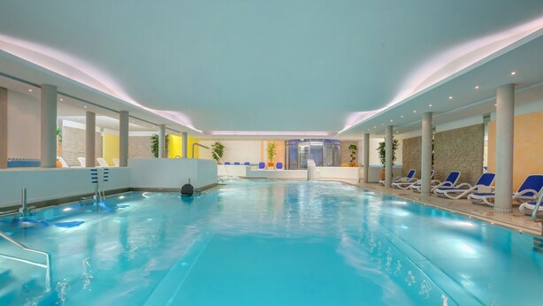 Una piscina interior con agua cristalina, rodeada de sillones de descanso y una zona de recepción.