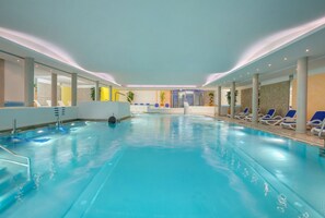 Una piscina interna con acqua cristallina, circondata da lettini e un’area reception.